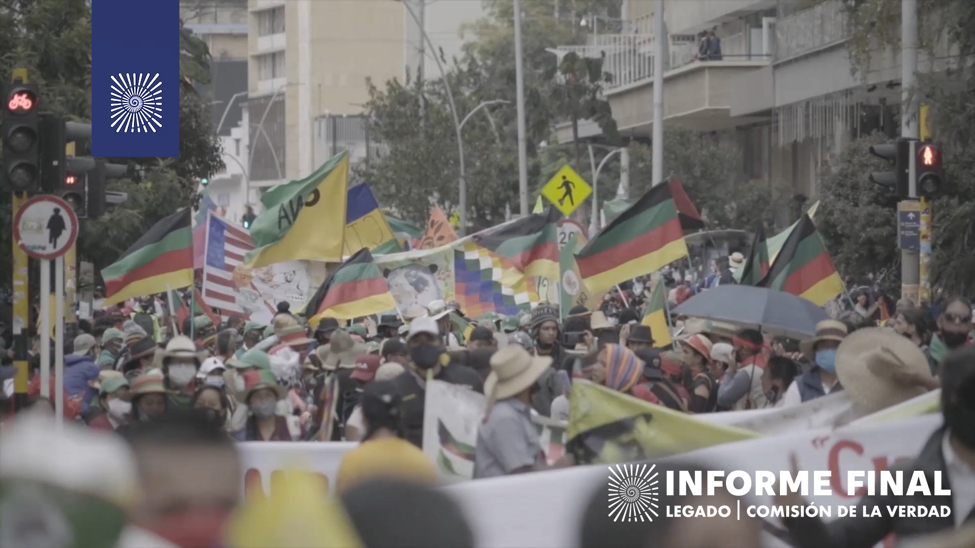 Multitud indígena, algunos con sombreros y tapabocas, alzan múltiples banderas.