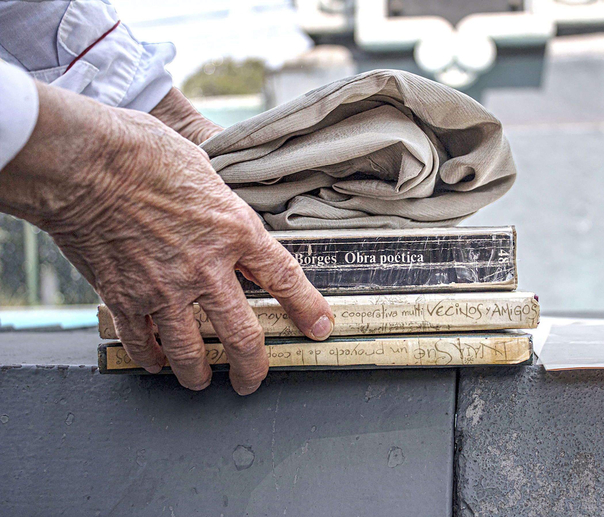 Un hombre anciano sostiene 3 libros y una chaqueta doblada. Detalle manos