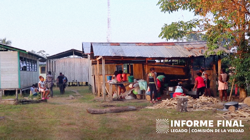 Varias mujeres fotografiadas realizando labores de cocina en exterior, algunos jóvenes observan y caminan cerca