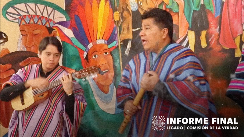 Dos músicos vistiendo poncho colorido realizando presentación musical, cantando y tocando instrumentos