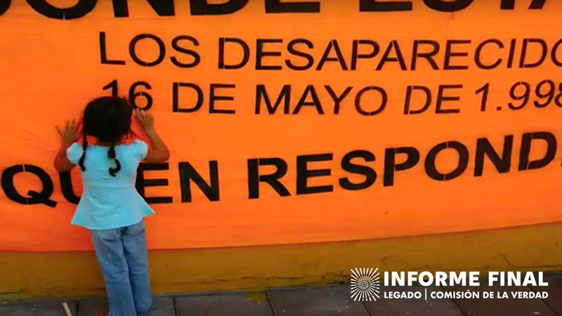 Niña con trenzas frente a mural textil naranja con textos "LOS DESAPARECIDOS" "16 DE MAYO DE 1.998"