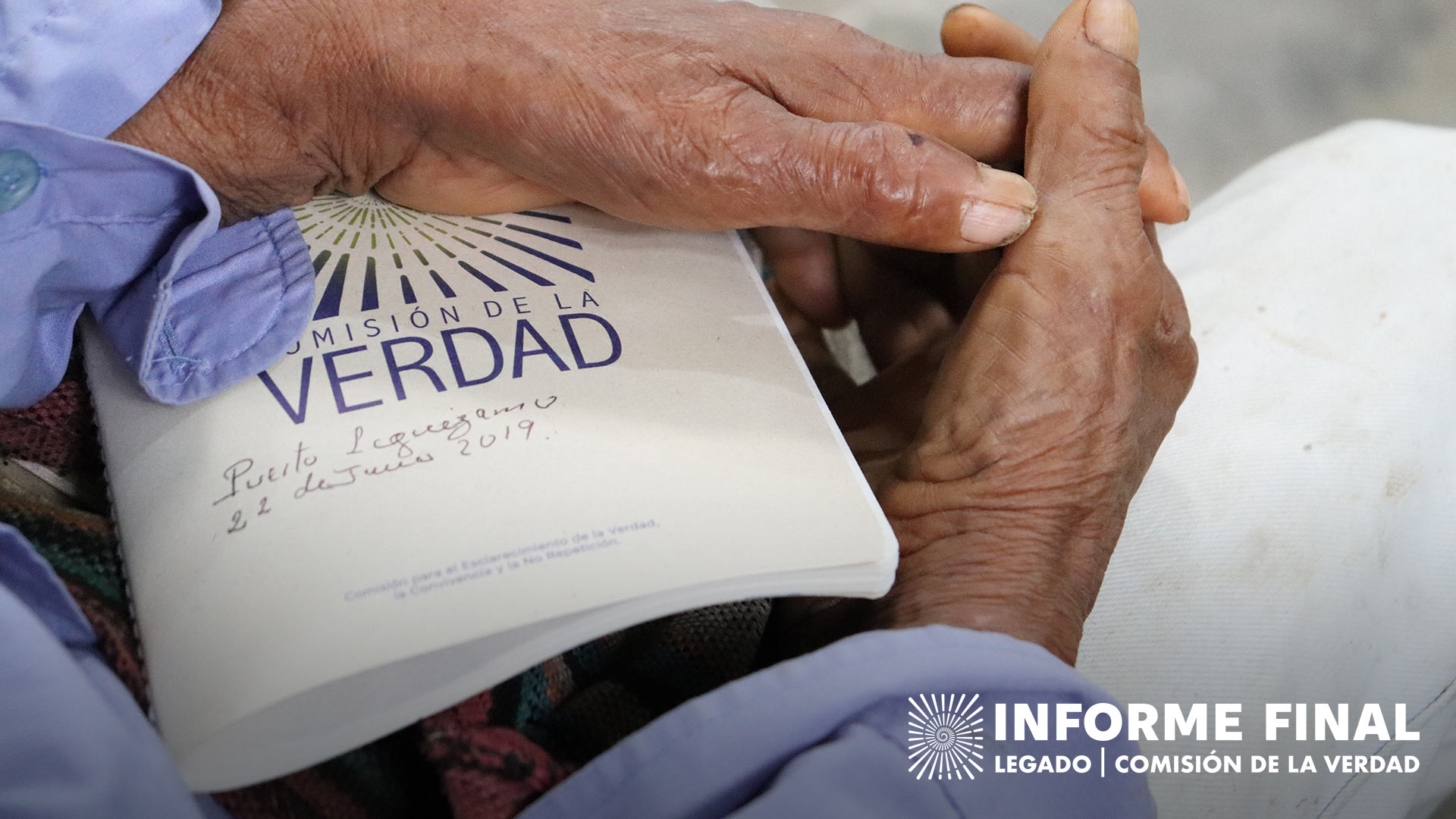 Manos de anciano sosteniendo un libro con el logo de la Comisión de la Verdad