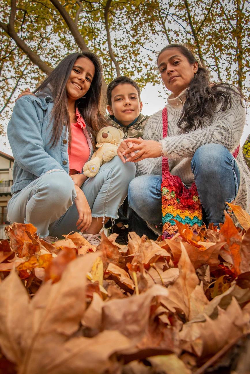 dos mujeres y un niño acurrucados sonriendo en medio de hojas secas y árboles