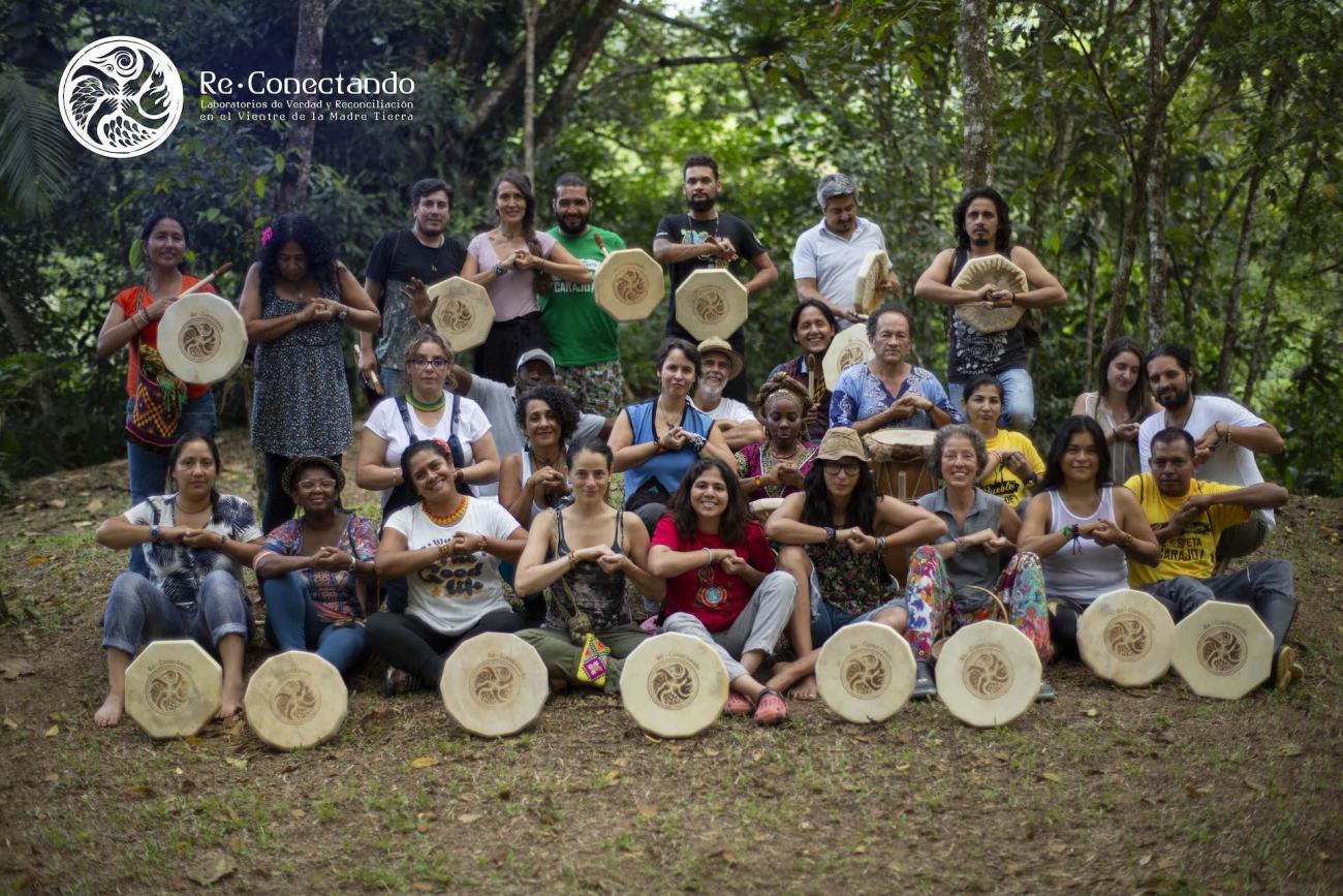 Grupo de personas con tambores sonríen y muestran un gesto al estrechar cada uno sus propias manos