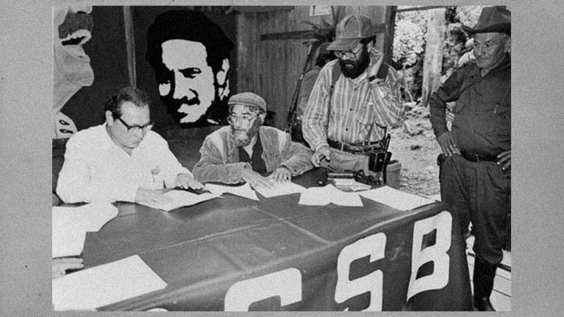 En blaco y negro, fotografiados antigos militantes de guerrilla discutiendo al rededor de una mesa