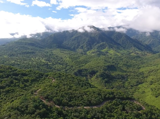 Paisaje donde se ve mucha vegetación, montañas, el cielo iluminado y muchas nubes